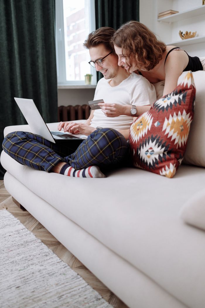 gallery-01 Happy couple sitting on a couch, using a laptop for online shopping with a credit card in hand.